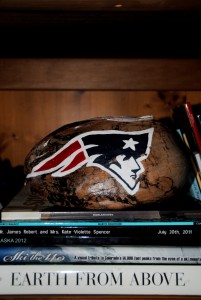 The current center piece for our living room. A Hawaiian coconut painted with the Patriots logo. Below that, a series of books from Colorado, Hawaii, and Alaska.